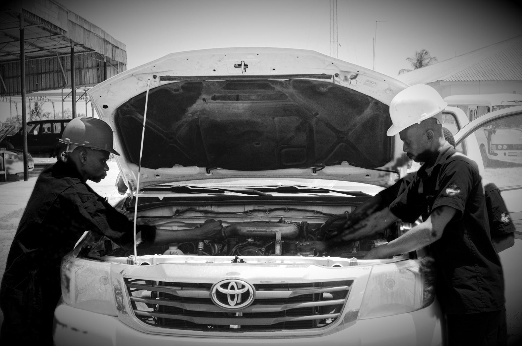 Two mechanics in black working under the bonnet of a bakkie